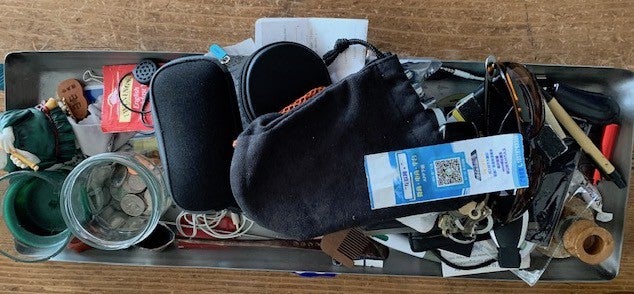 Collection of objects: a wallet, a glass with coins, a case of glasses, keys, pens, earplugs, and others