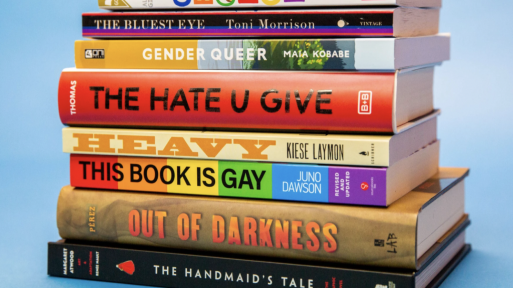 Pile of banned books. The titles include: Toni Morrison's The Bluest Eye, Maia Kobabe's Gender Queer, Thomas' The Hate U Give, Kiese Laymon's Heavy, Juno Dawson's This Book is Gay, Pérez's Out of Darkness, and Atwood's The Handmaiden's Tale