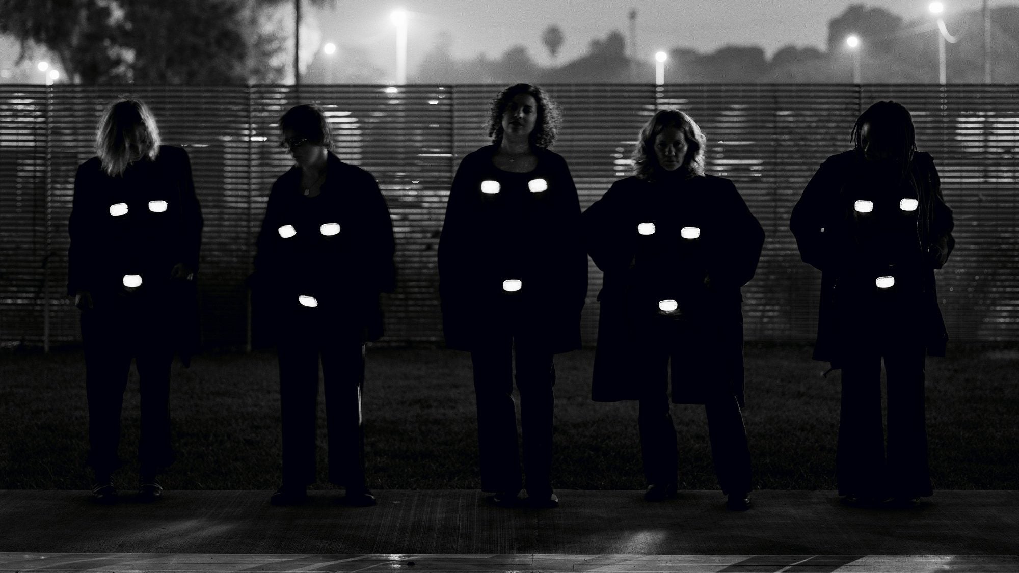 Black and white picture featuring a group of women in the city at night, with lightboxes on top of their breast and vaginas