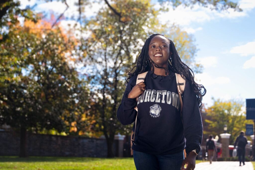 A student wearing a Georgetown sweatshirt walks outside smiling.